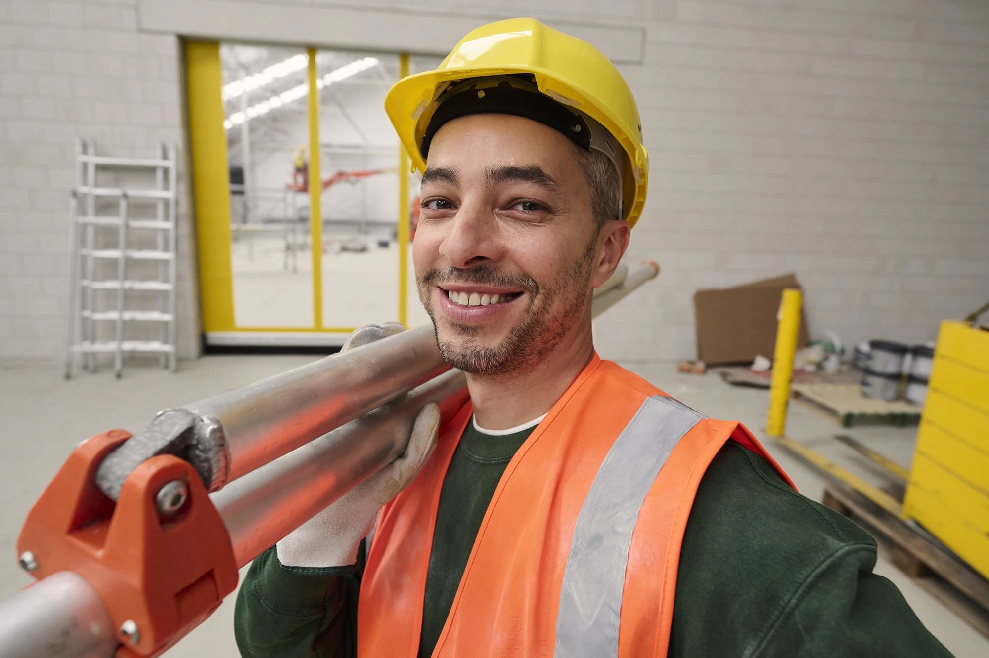 Trabalhador da construção com capacete e colete fluorescente sorri no estaleiro — empregos na construção através da Accent