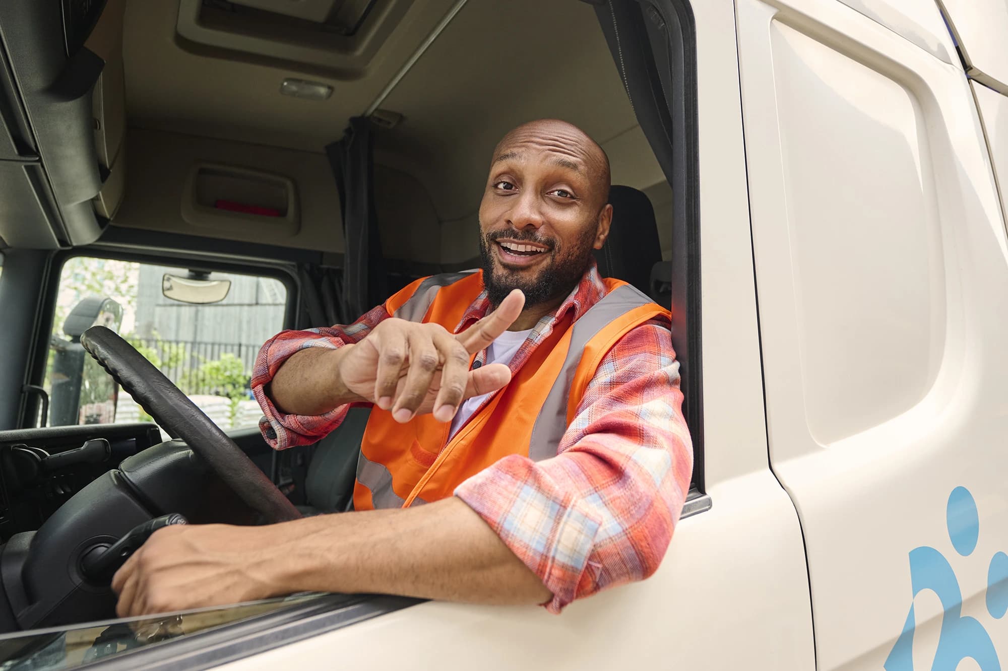 Motorista de camião com colete fluorescente sorri e aponta a partir da cabine — empregos em transportes via Accent